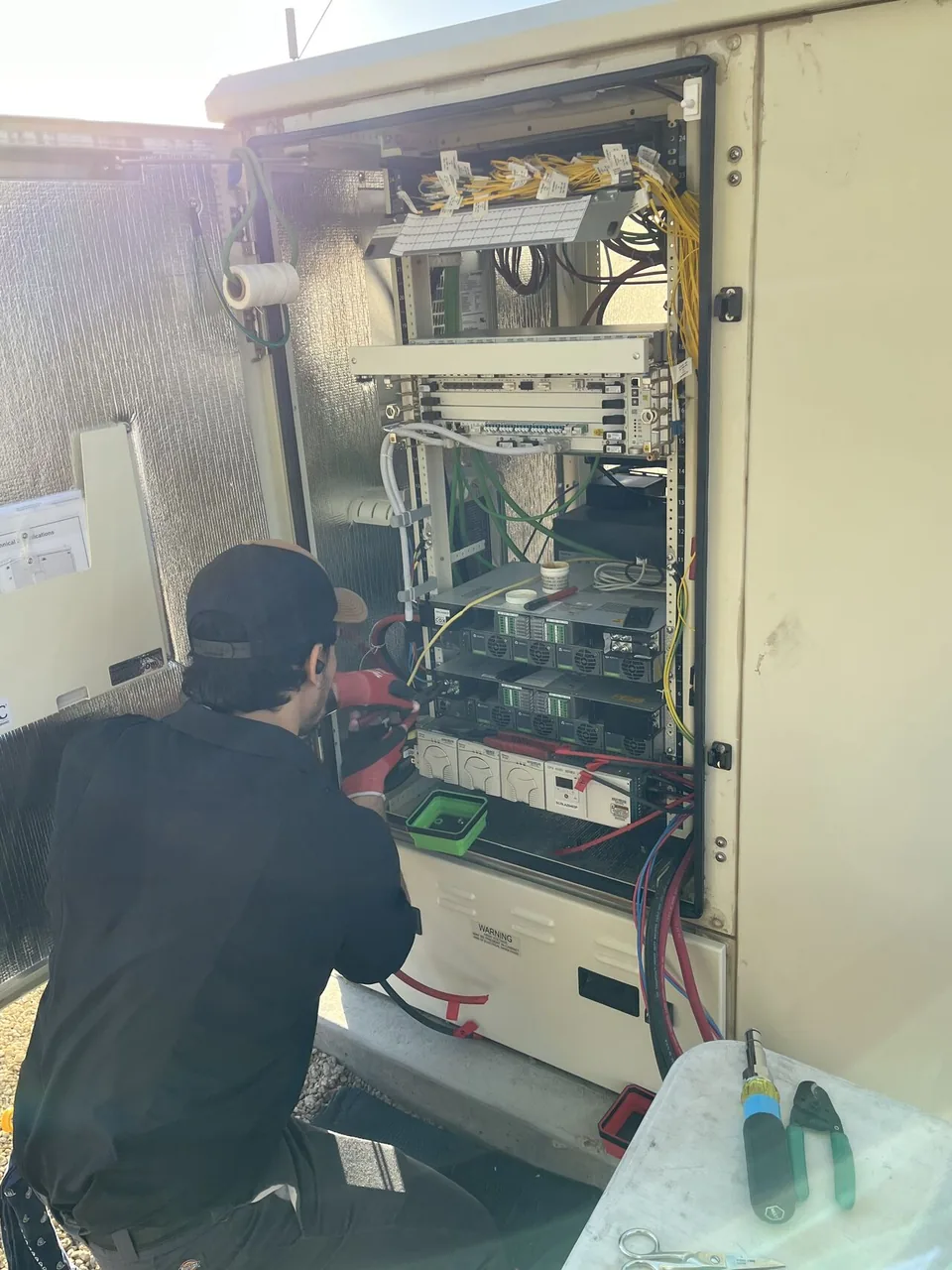 New Phase technician working on outdoor telecom cabinet with rectifiers, Arizona
